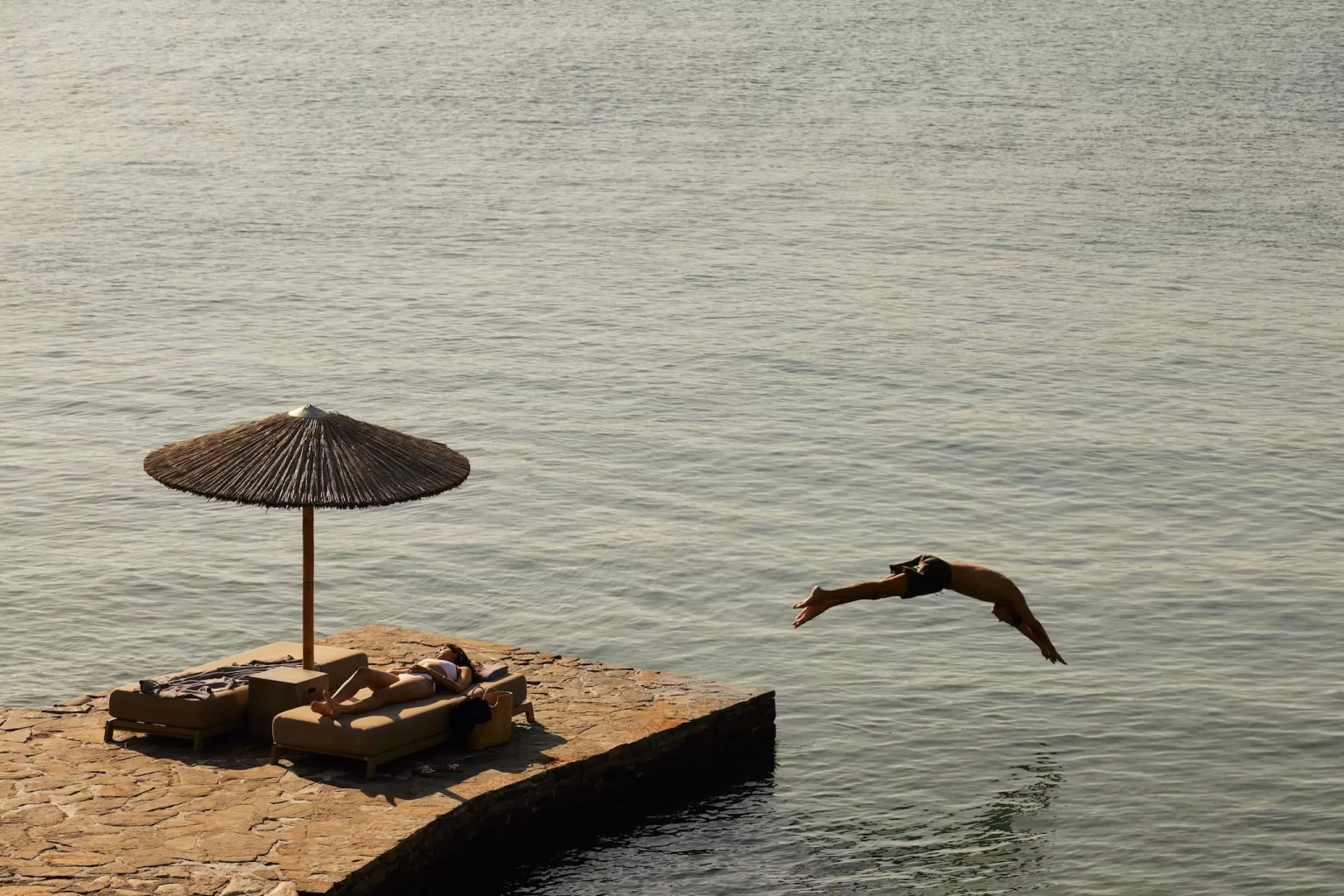 Man diving from a stone pier into the sea at Minos Beach Art Hotel.