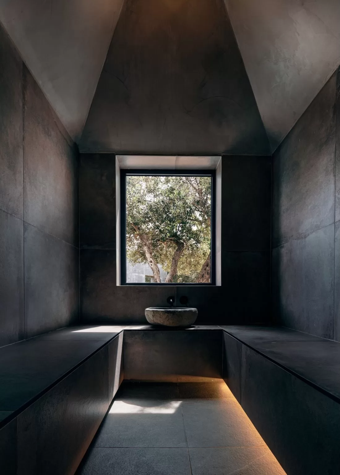 Dark stone spa room at Minos Beach Art Hotel with a central window framing an olive tree.