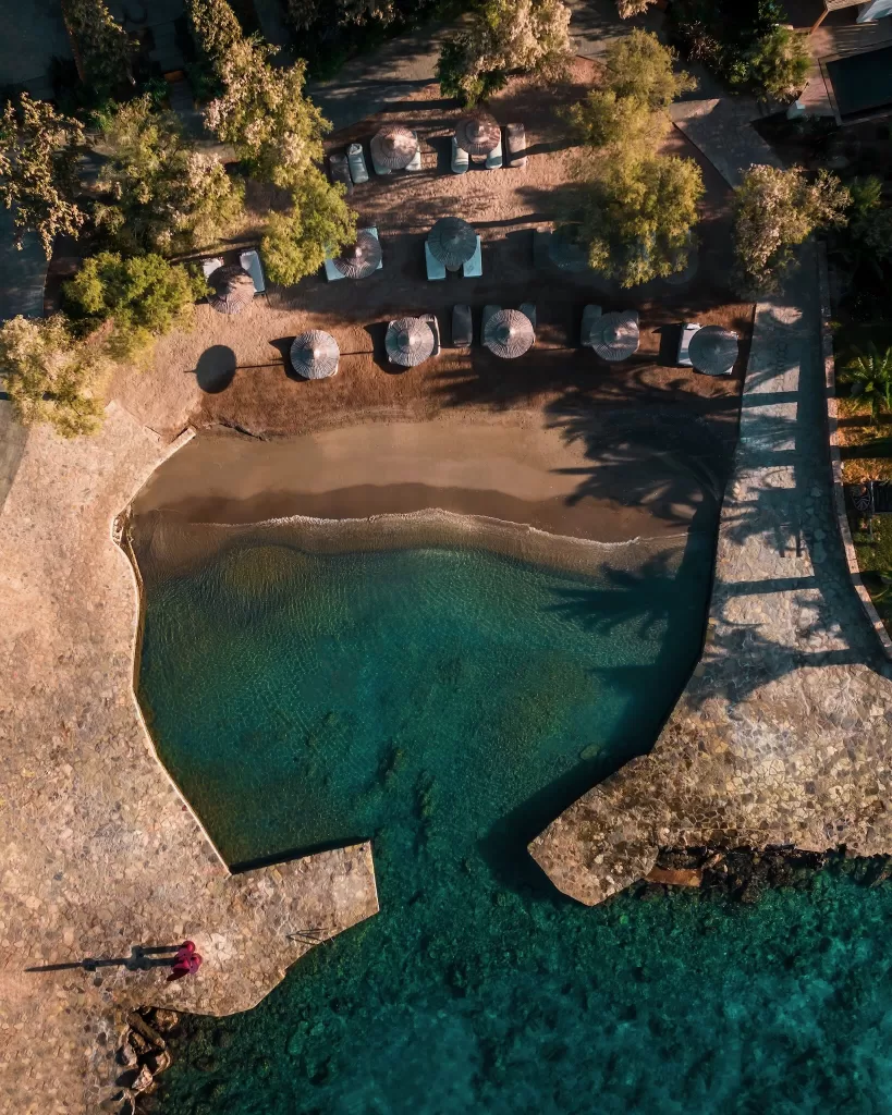 Aerial view of a secluded sandy cove with sun loungers and umbrellas at Minos Beach Art Hotel.