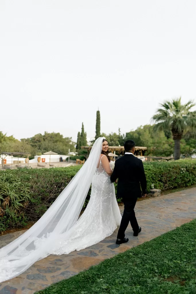 Bride smiling over her shoulder while walking hand-in-hand with groom at Minos Beach Art Hotel.
