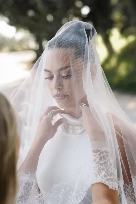 Bride in lace-edged veil adjusting her gown before the ceremony at Minthis Resort.