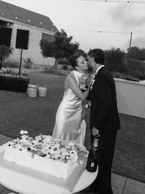 Black and white photo of newlyweds sharing a kiss beside their wedding cake at Minthis Resort.