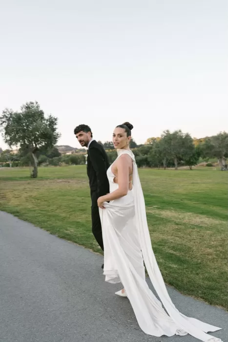 Bride and groom walking hand in hand on a paved path at Minthis Resort, the bride glancing back.
