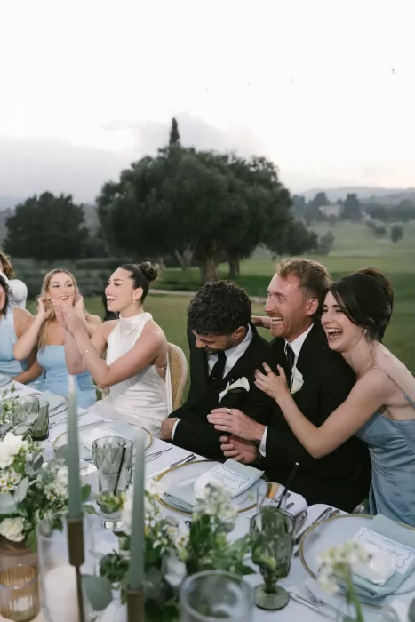 Bride, groom, and guests laughing together at the wedding reception table at Minthis Resort.