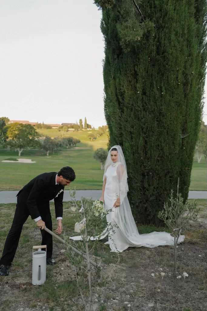 Groom planting a tree while the bride watches during an outdoor ceremony at Minthis Resort.