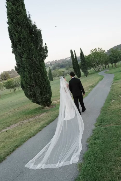 Bride and groom walking away along a path, the bride’s lace-trimmed veil trailing behind at Minthis Resort.