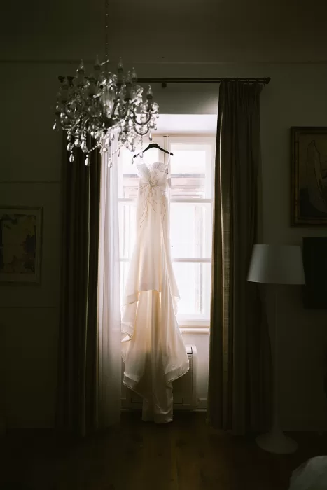 Wedding dress hanging by a window with soft natural light inside the Museum of Modern Art Dubrovnik.