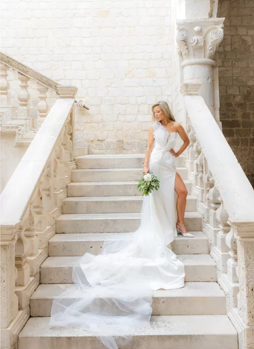 Bride holding bouquet while posing on elegant stone staircase at the Museum of Modern Art Dubrovnik.