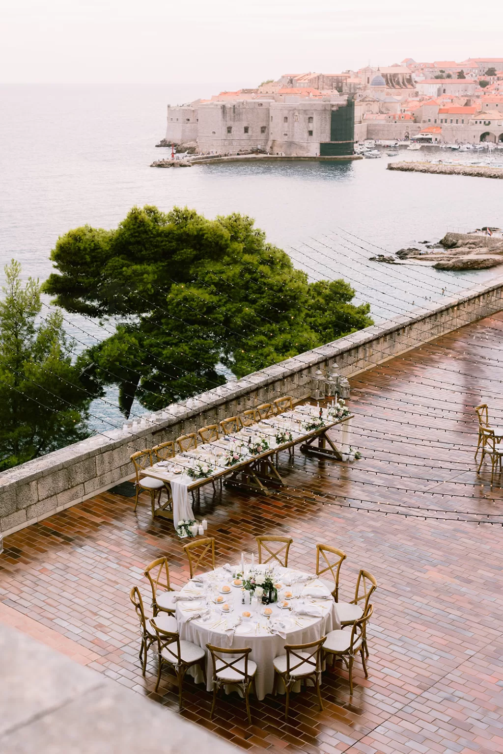 Wedding dinner tables set on the terrace of the Museum of Modern Art Dubrovnik overlooking the Adriatic Sea and city walls.