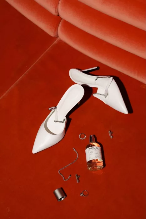 Bridal accessories including white heels, perfume, and jewellery arranged on a rich red surface.