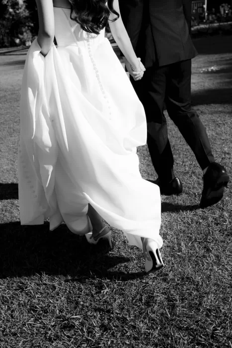 Bride lifting her gown as she walks hand in hand with the groom across the grass at Next Chapter Events.