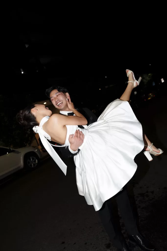 Groom lifting the bride in her short reception dress at night, both laughing joyfully outside Next Chapter Events.
