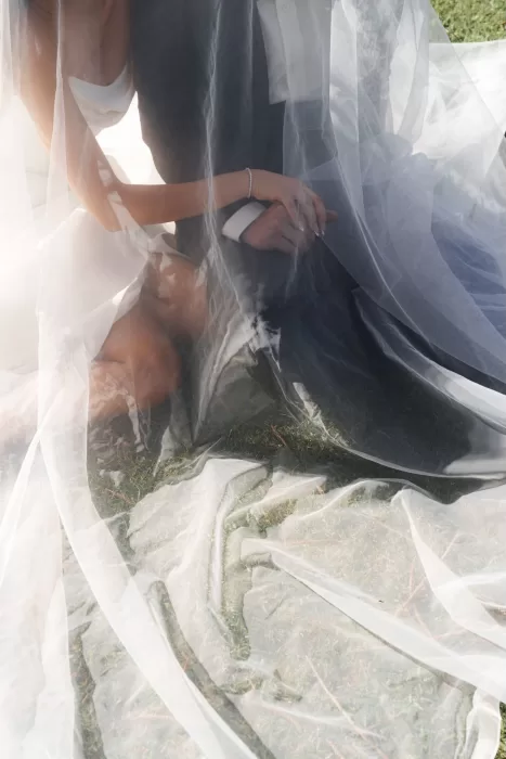 Bride and groom seated under a flowing veil, holding hands in an intimate and romantic moment at Next Chapter Events.