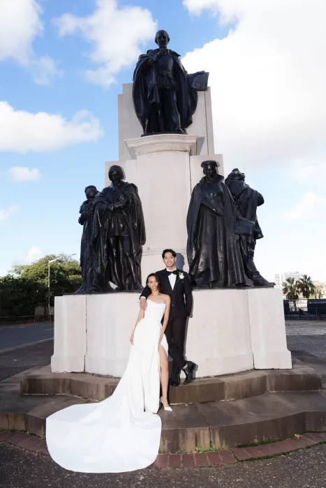 Bride and groom posing by a grand monument near Next Chapter Events, the bride’s gown cascading onto the stone platform.
