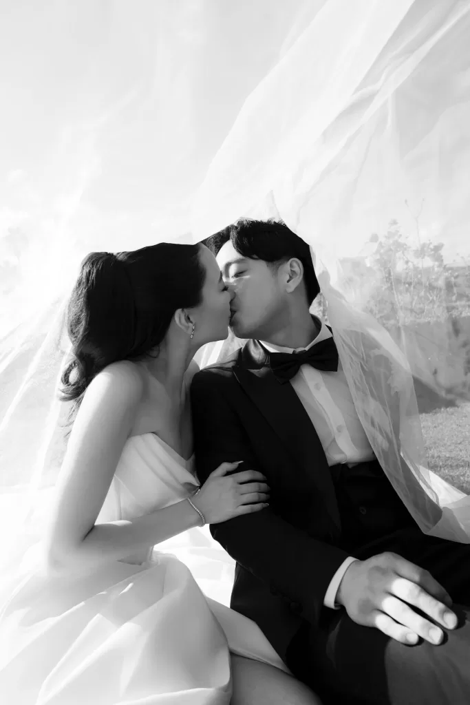 Bride and groom sharing a kiss under the bridal veil in soft natural light.