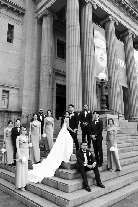Wedding party posing on the grand steps of Next Chapter Events with elegant columns in the background.