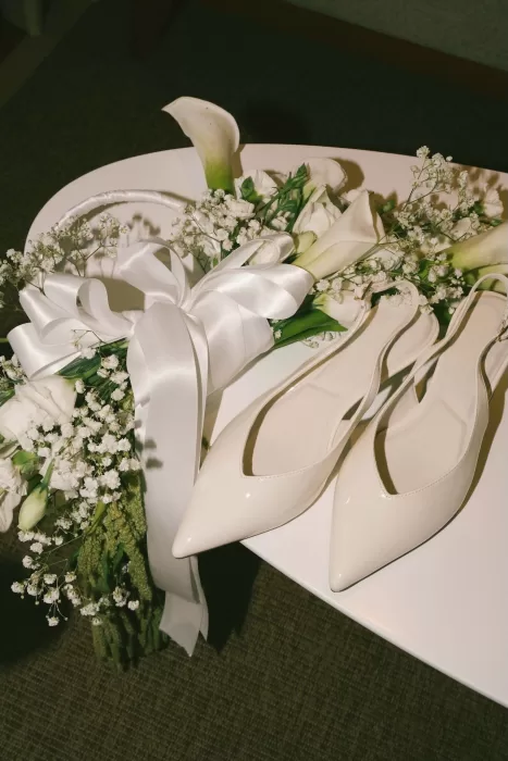 Bridal bouquet of white flowers with satin ribbon placed beside ivory wedding shoes at Padma Resort Legian.