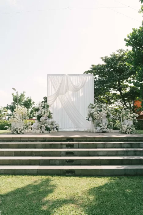 White draped ceremony backdrop with lush floral arrangements on stone steps at Padma Resort Legian.