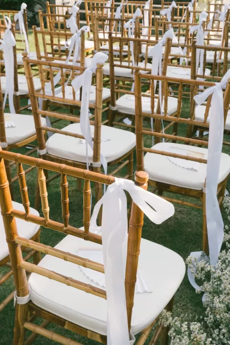Wooden ceremony chairs tied with white ribbons and paper fans for guests at Padma Resort Legian.