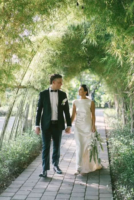 Bride and groom walking hand in hand beneath a bamboo archway at Padma Resort Legian.