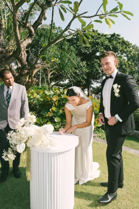 Bride and groom signing wedding documents outdoors surrounded by flowers at Padma Resort Legian.