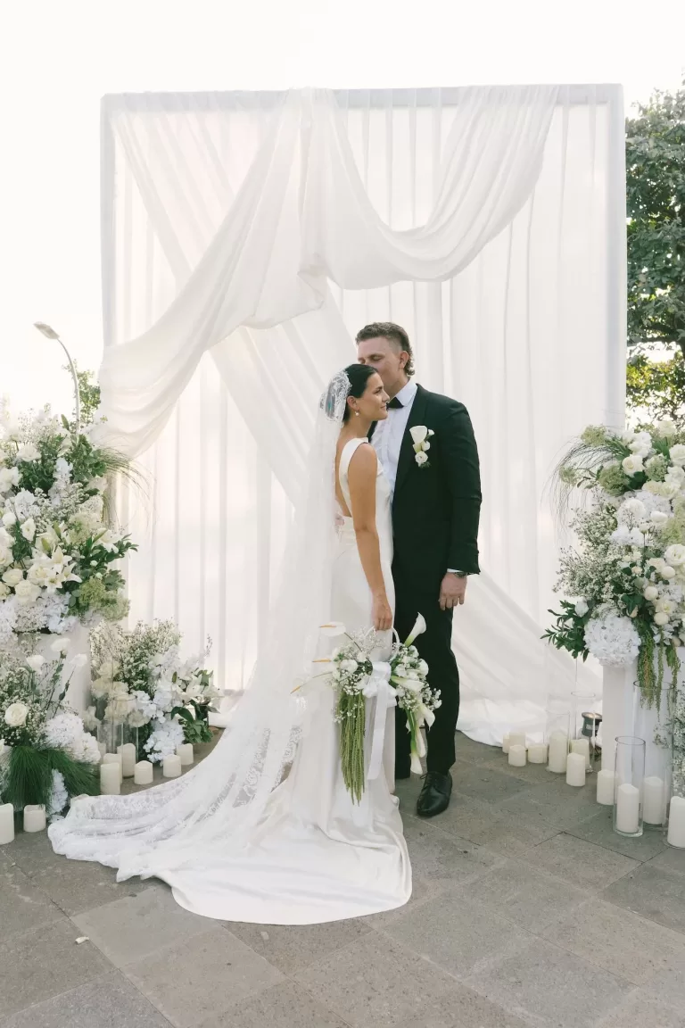 Bride and groom embracing under a romantic white draped altar at Padma Resort Legian.