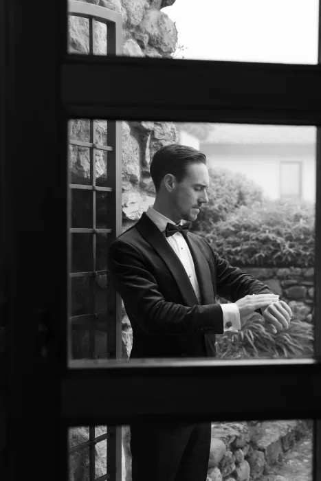 Groom in a tuxedo adjusting his cufflinks while preparing for the wedding at Rustico Bertel.