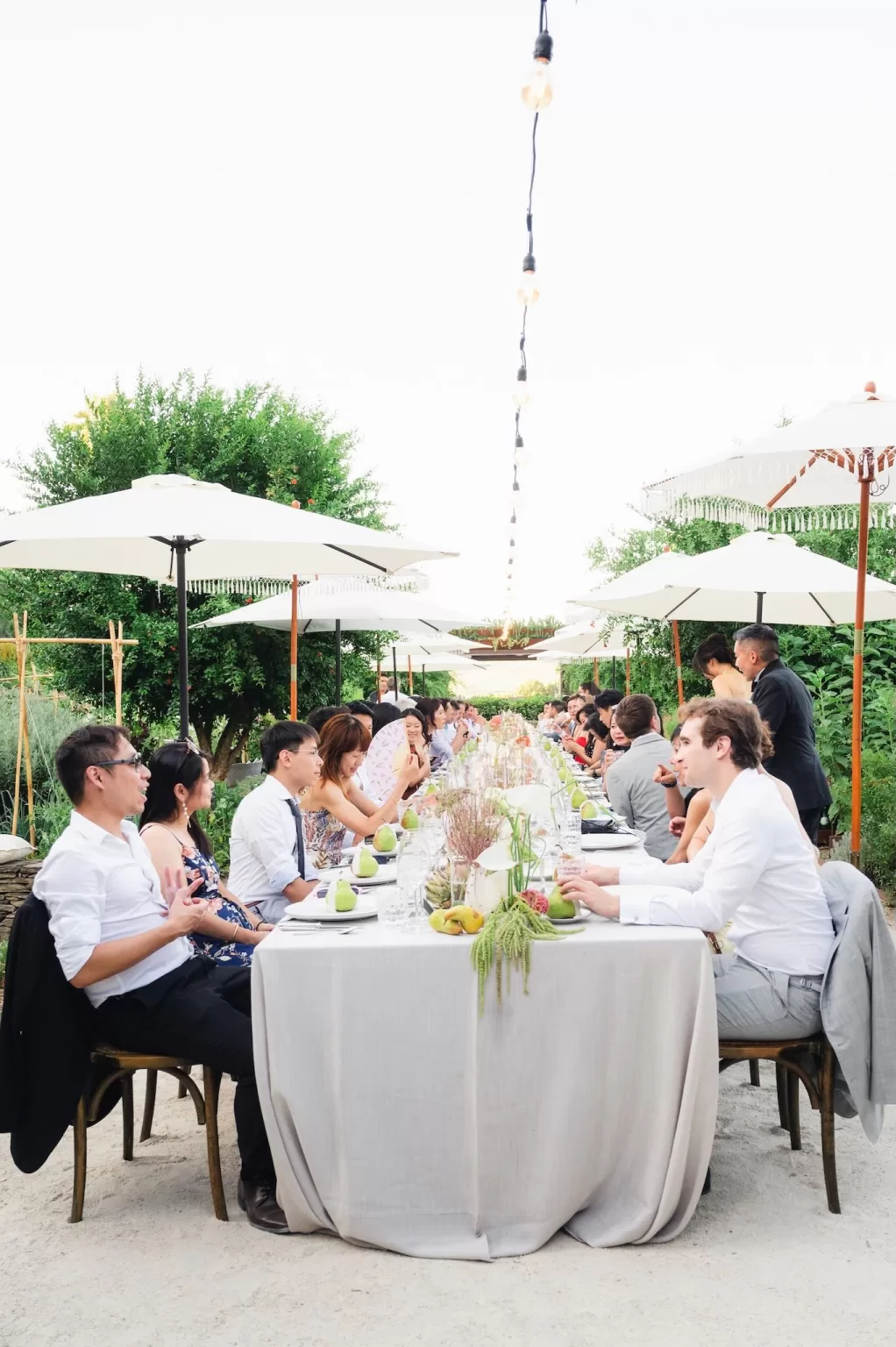 Outdoor wedding dinner in the gardens with elegant long tables and white umbrellas at Six Senses Douro Valley.