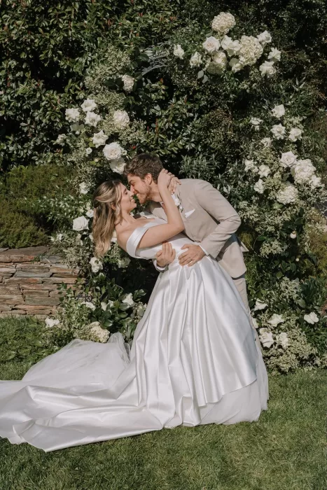 Groom dipping bride for a kiss in front of floral arch at Six Senses Douro Valley