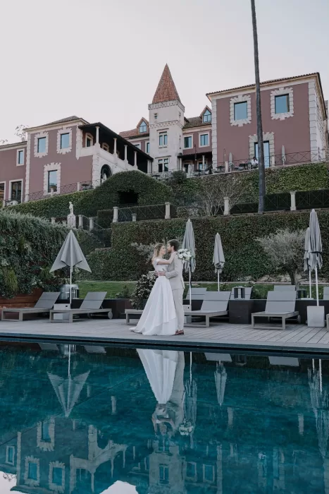 Bride and groom embracing by the pool with villa reflection at Six Senses Douro Valley.