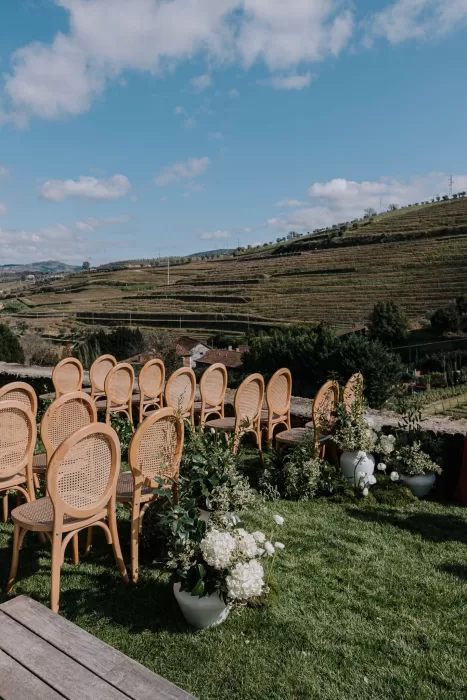 Outdoor wedding ceremony setup with wooden chairs and white flowers overlooking Douro Valley vineyards.