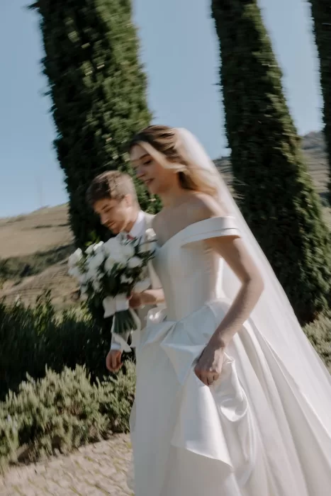 Bride and groom walking hand in hand past cypress trees at Six Senses Douro Valley.