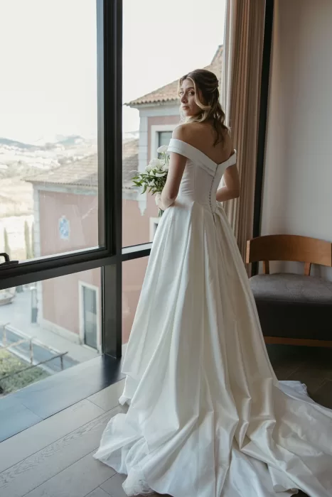 Bride holding bouquet in front of window with sweeping gown at Six Senses Douro Valley.