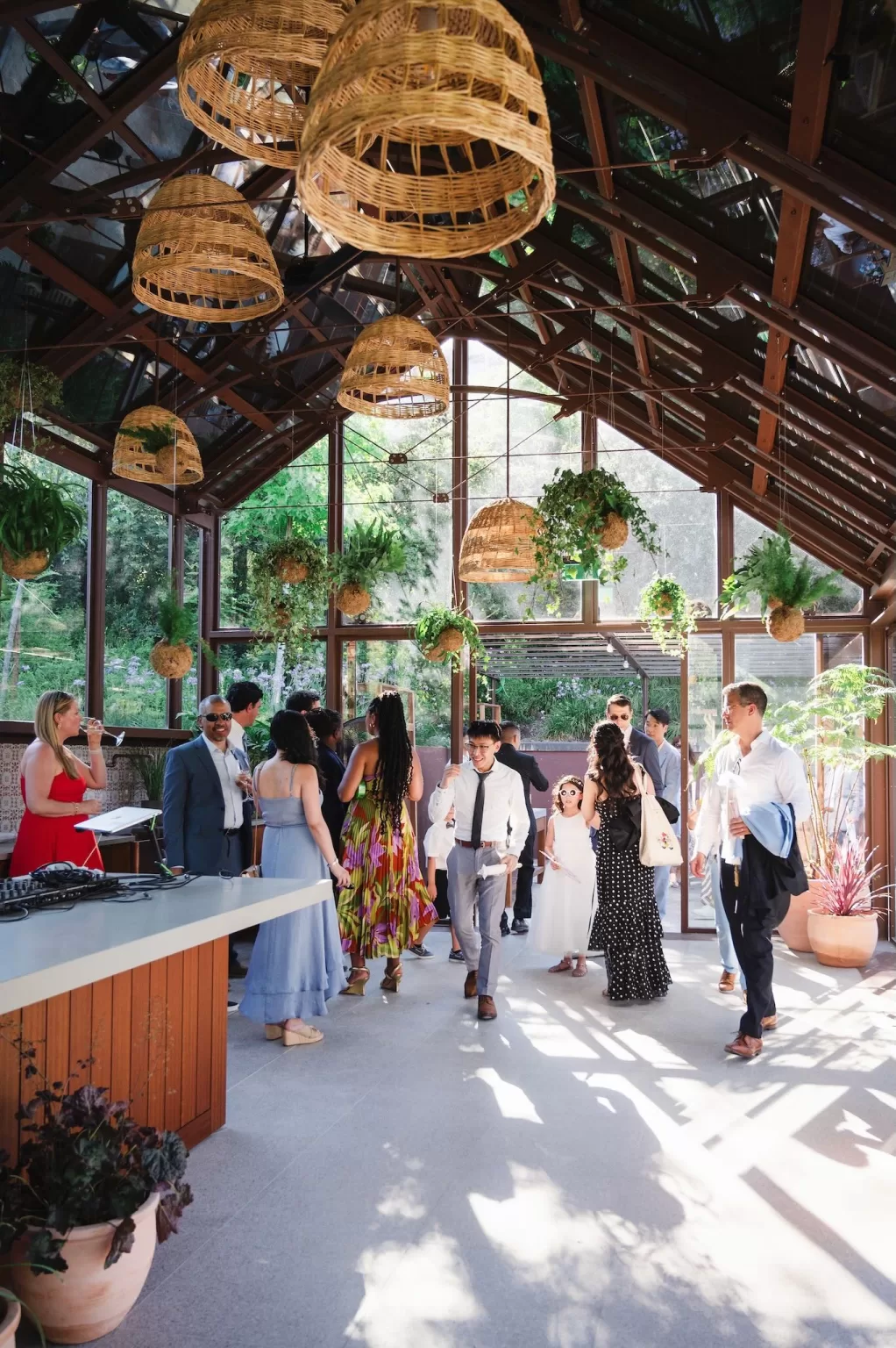 Guests enjoying a cocktail reception inside a glasshouse with rattan lights and hanging greenery at Six Senses Douro Valley.