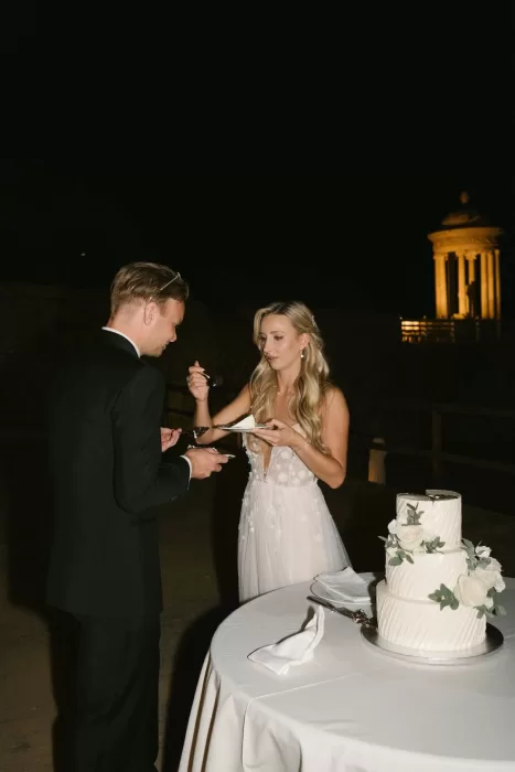 Bride and groom sharing a slice of wedding cake at Son Marroig with the illuminated pavilion glowing in the background.