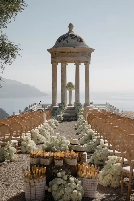 Elegant ceremony setup at Son Marroig with rattan chairs and white floral aisle leading to the marble pavilion overlooking the sea.