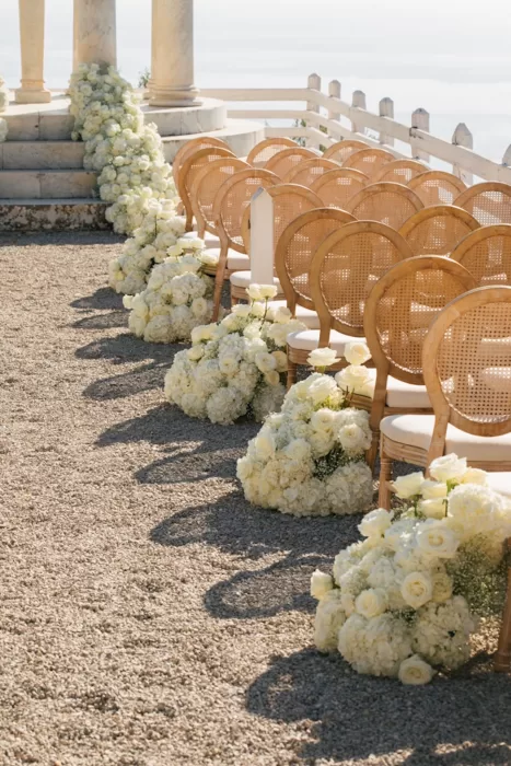 Ceremony aisle at Son Marroig lined with wooden chairs and clusters of white roses and hydrangeas.