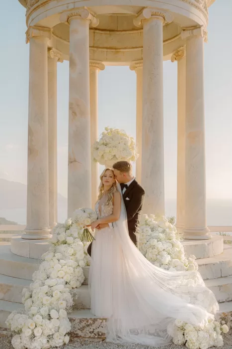 Bride and groom embracing beneath the marble pavilion at Son Marroig surrounded by lush floral arrangements.