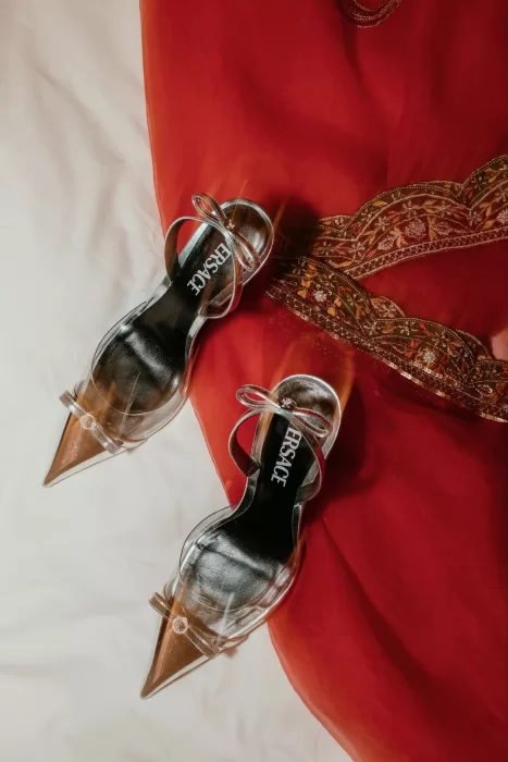 Metallic Versace heels resting against a red embroidered bridal lehenga.