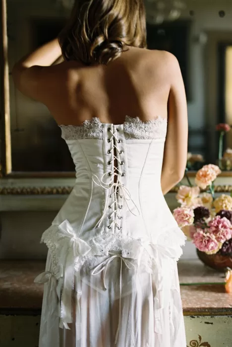 Bride wearing a delicate lace corset with ribbon details during bridal preparations at Villa Arvedi.