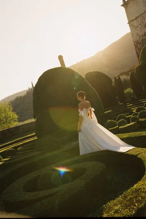 Bride in flowing gown standing among the manicured gardens of Villa Arvedi at golden hour.