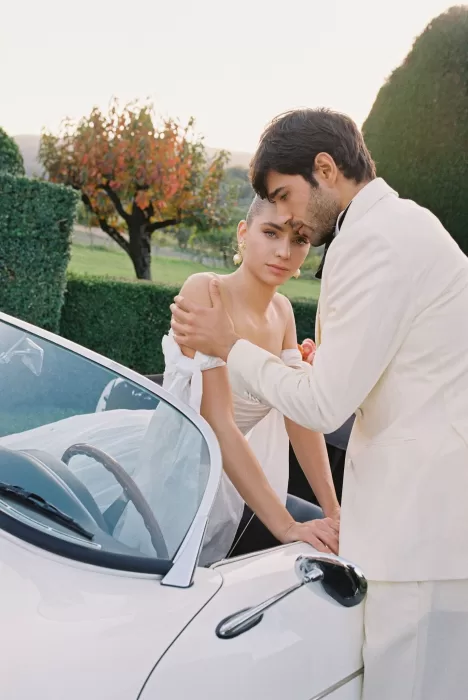 Groom embraces bride tenderly beside a vintage white convertible at Villa Arvedi.