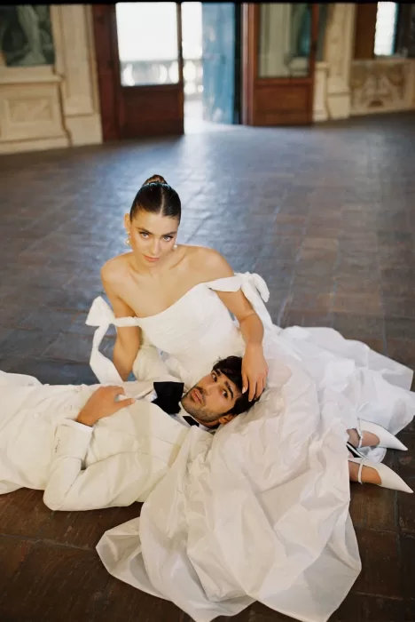 Bride and groom in white attire seated on the floor of Villa Arvedi’s grand hall.