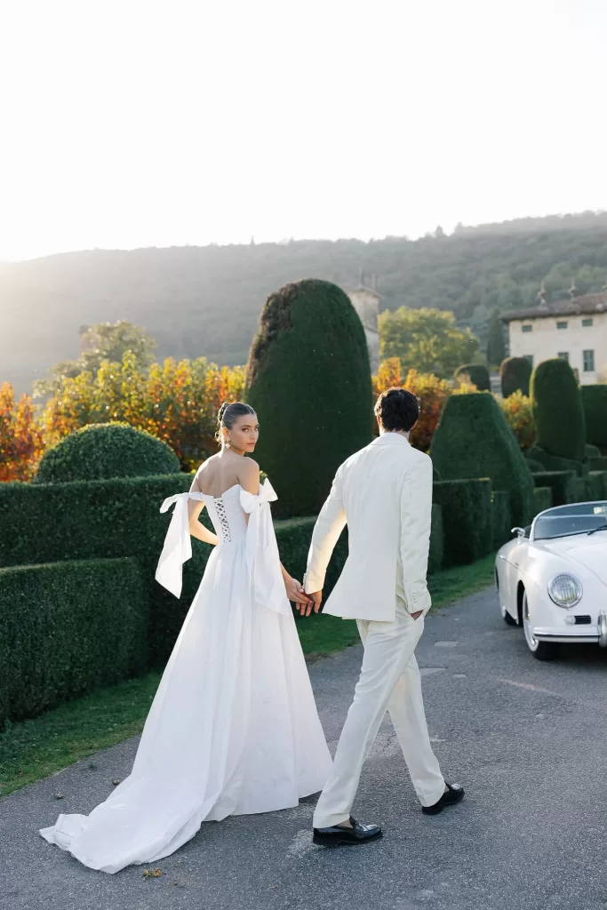 Couple holding hands while walking past a vintage car in Villa Arvedi gardens.