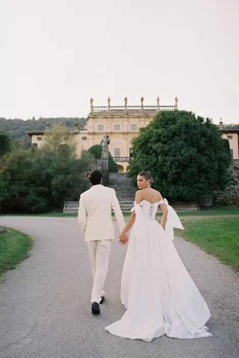 Bride and groom walking hand in hand toward Villa Arvedi’s historic façade.