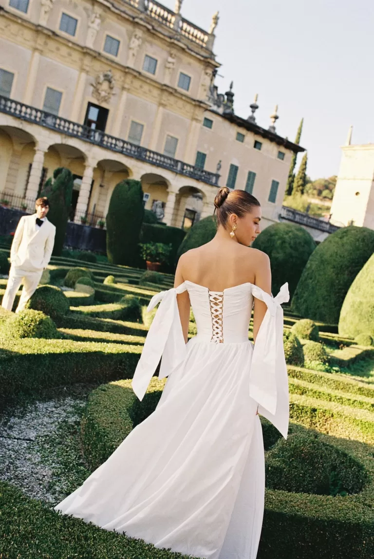 Bride in lace-up gown walking through the manicured gardens of Villa Arvedi.