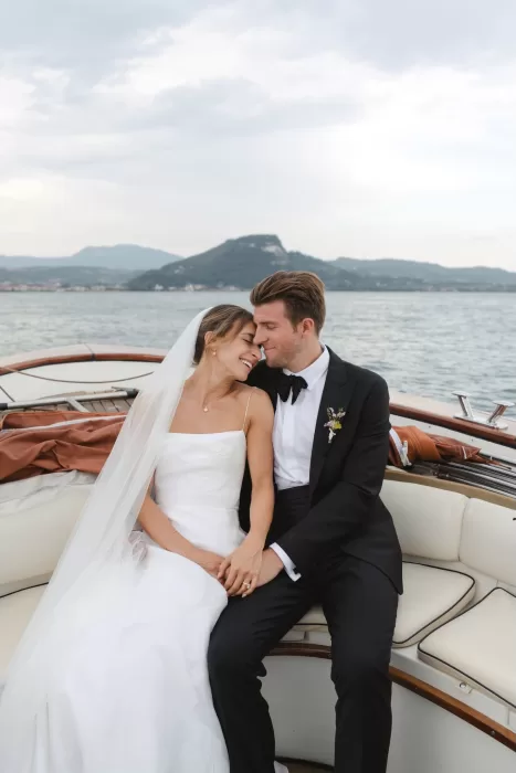 Bride and groom share a quiet moment on a boat after their Villa San Vigilio wedding ceremony, with lake and mountains in the background.