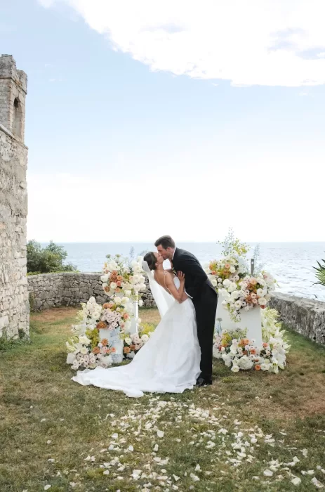 The couple shares a kiss by the water’s edge surrounded by pastel florals during their Villa San Vigilio ceremony.