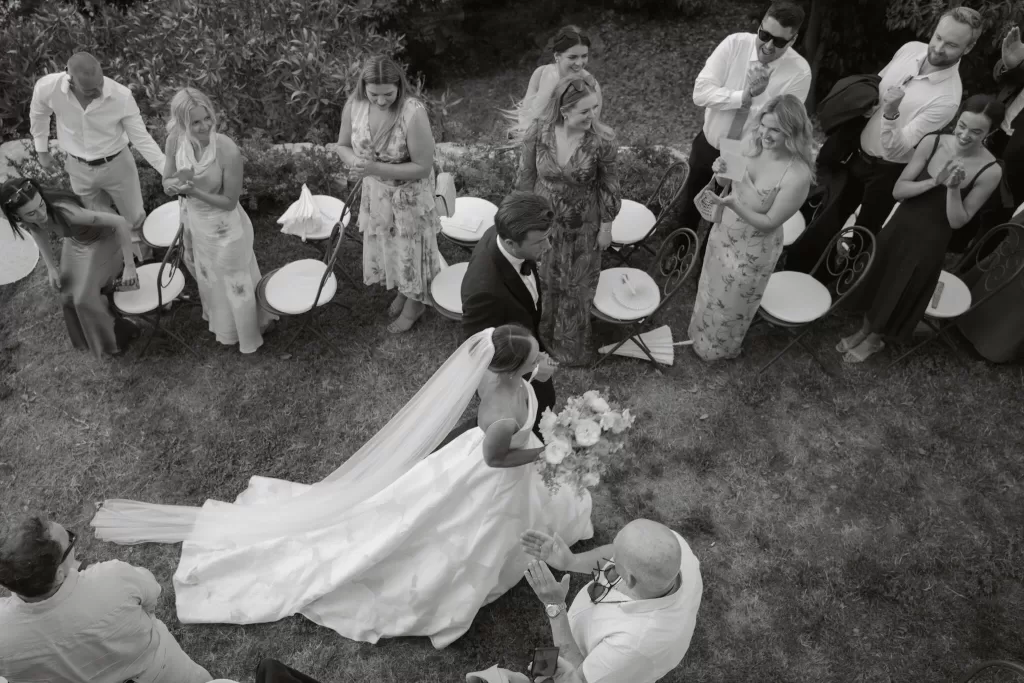 Bride and groom walk down the aisle at Villa San Vigilio surrounded by applauding guests in a candid overhead shot.