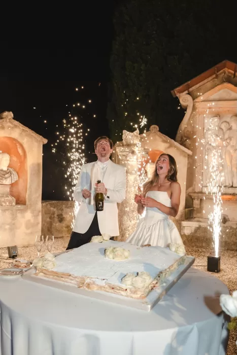 Bride and groom pop champagne amid sparklers at their Villa San Vigilio wedding celebration, full of joy and laughter.